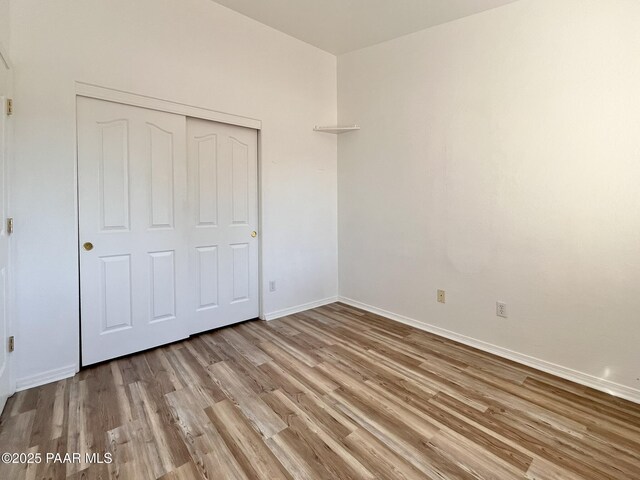 unfurnished bedroom featuring light wood finished floors, a closet, and baseboards