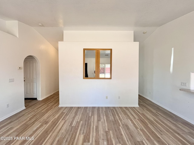 unfurnished room with arched walkways, vaulted ceiling, light wood-style flooring, and baseboards