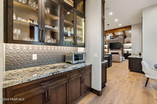 bar with light stone countertops, decorative light fixtures, light hardwood / wood-style flooring, beamed ceiling, and a fireplace