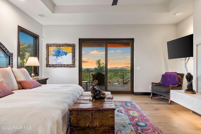 bedroom with access to exterior, light wood-type flooring, a tray ceiling, and ceiling fan