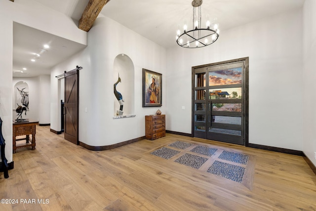 interior space featuring a barn door, light wood-type flooring, beam ceiling, and an inviting chandelier