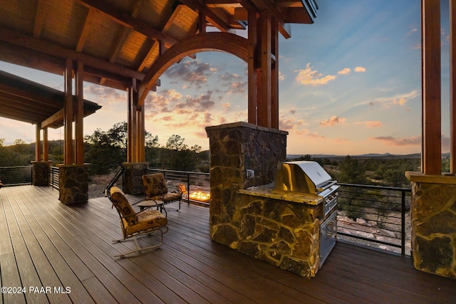 deck at dusk with an outdoor kitchen and area for grilling