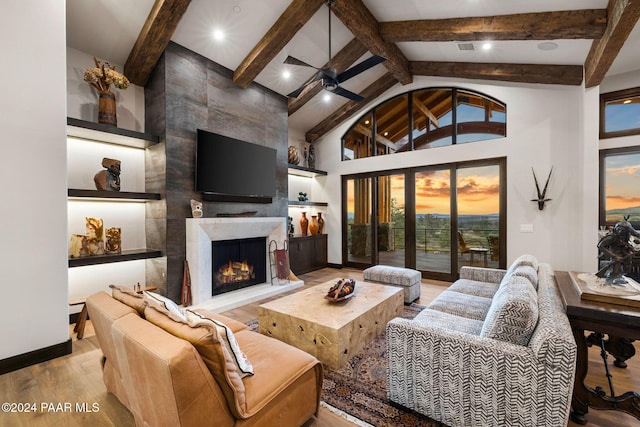 living room featuring beam ceiling, ceiling fan, a high end fireplace, high vaulted ceiling, and light wood-type flooring