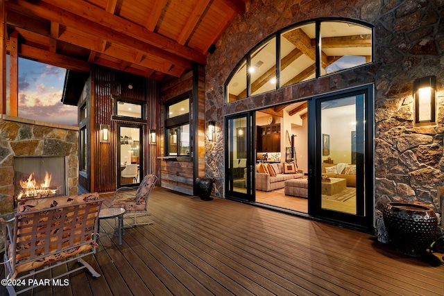 deck at dusk featuring an outdoor stone fireplace