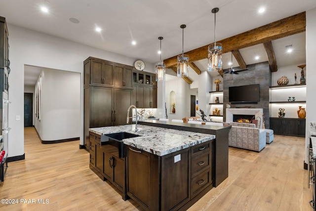 kitchen featuring dark brown cabinetry, a kitchen island with sink, sink, and beamed ceiling