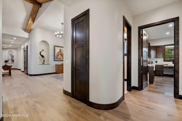 hallway with beamed ceiling, light wood-type flooring, a barn door, and a chandelier