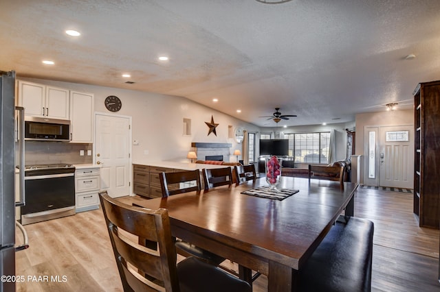 dining space with ceiling fan, lofted ceiling, light hardwood / wood-style floors, and a textured ceiling