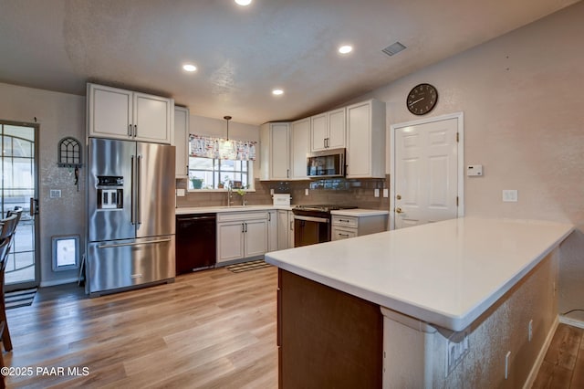 kitchen featuring stainless steel appliances, hanging light fixtures, white cabinets, and kitchen peninsula