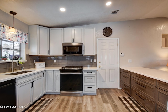 kitchen featuring appliances with stainless steel finishes, pendant lighting, white cabinetry, sink, and light hardwood / wood-style flooring