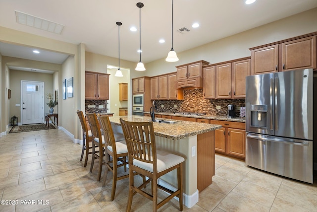 12691 E De La Cruz St, Dewey-Humboldt, AZ 86327 - kitchen with stainless steel appliances, decorative backsplash, brown cabinetry, a kitchen island with sink, and recessed lighting