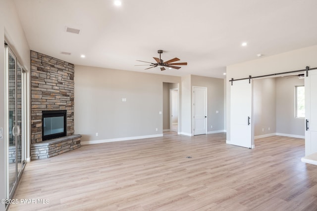 unfurnished living room with a barn door, ceiling fan, light wood-style floors, baseboards, and a fireplace