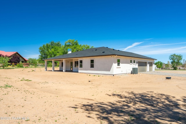rear view of property featuring cooling unit, stucco siding, an attached garage, and driveway