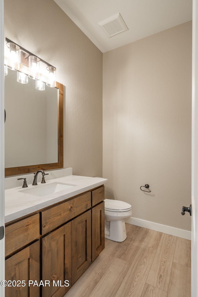 bathroom with wood finished floors, toilet, vanity, and baseboards