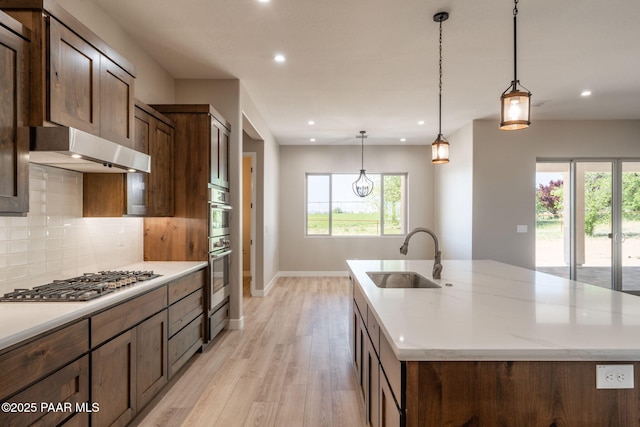 kitchen featuring a sink, stainless steel gas stovetop, under cabinet range hood, light wood finished floors, and baseboards