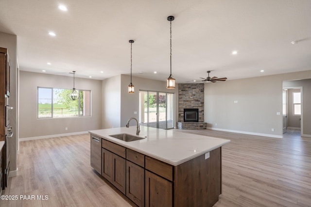 kitchen featuring a sink, a ceiling fan, stainless steel dishwasher, a fireplace, and light wood finished floors