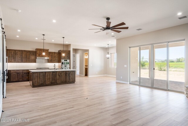 kitchen featuring double oven, light countertops, recessed lighting, open floor plan, and a kitchen island with sink
