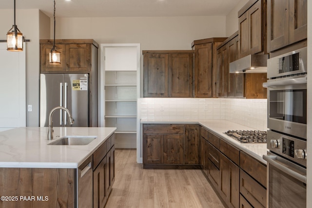 kitchen featuring appliances with stainless steel finishes, a sink, extractor fan, light wood-type flooring, and pendant lighting