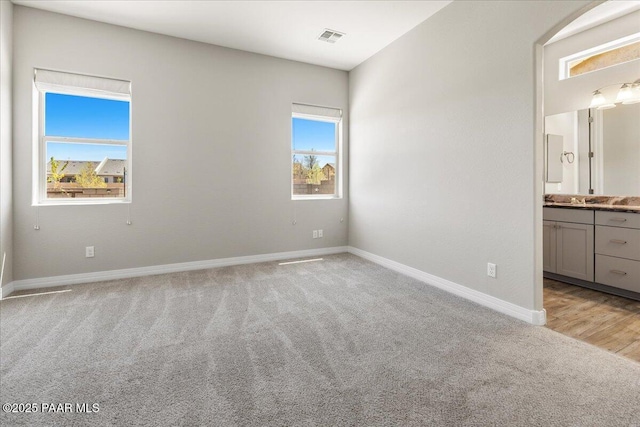 unfurnished bedroom with baseboards, visible vents, light colored carpet, and ensuite bathroom