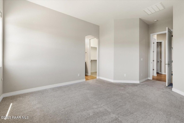 unfurnished bedroom with visible vents, light carpet, arched walkways, a walk in closet, and baseboards