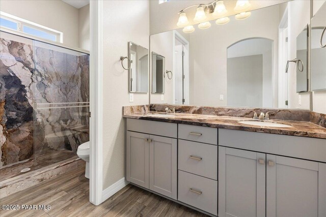 full bathroom featuring wood finished floors, a sink, a marble finish shower, and toilet