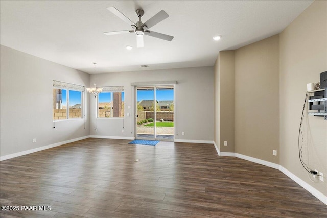 unfurnished room with ceiling fan with notable chandelier, baseboards, and dark wood-style flooring