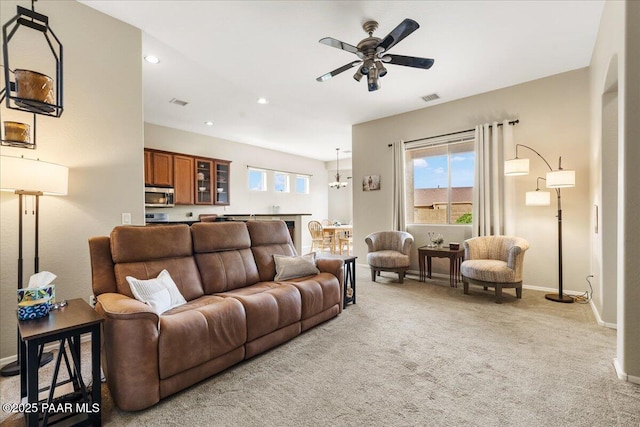 living room featuring ceiling fan with notable chandelier, visible vents, baseboards, light carpet, and recessed lighting