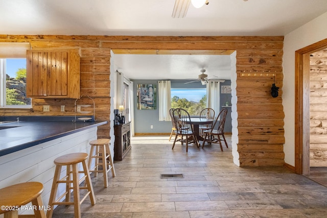 kitchen with a breakfast bar, rustic walls, ceiling fan, and light wood-type flooring