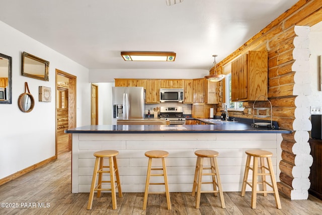 kitchen featuring appliances with stainless steel finishes, decorative light fixtures, kitchen peninsula, and a kitchen bar