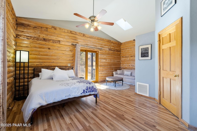 bedroom with wood-type flooring, vaulted ceiling with skylight, rustic walls, and ceiling fan