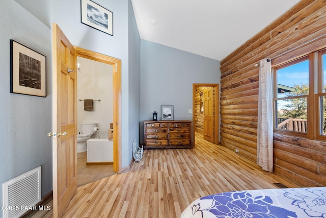 bedroom featuring hardwood / wood-style flooring, connected bathroom, rustic walls, and high vaulted ceiling