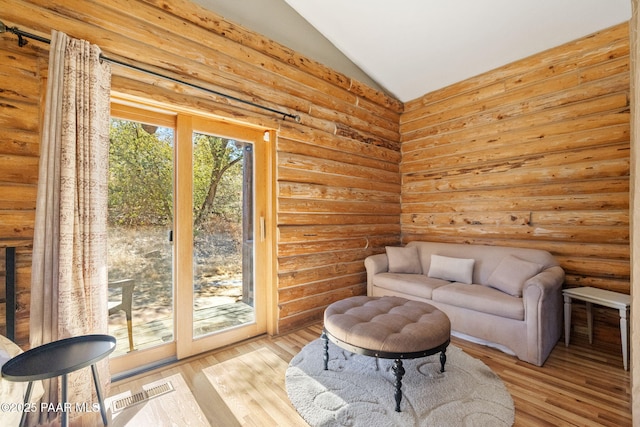 sitting room featuring vaulted ceiling, rustic walls, and light wood-type flooring