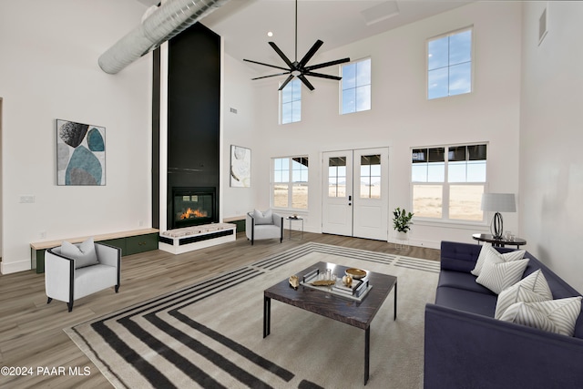 living room featuring ceiling fan, wood-type flooring, a fireplace, and a high ceiling