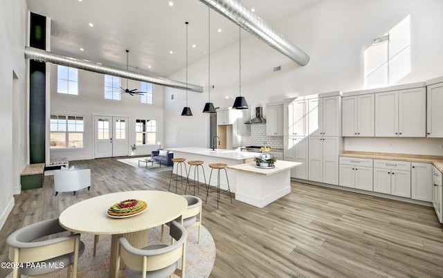 kitchen featuring a high ceiling, white cabinetry, an island with sink, hanging light fixtures, and ceiling fan