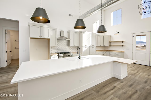 kitchen featuring white cabinetry, a spacious island, stove, wall chimney exhaust hood, and sink