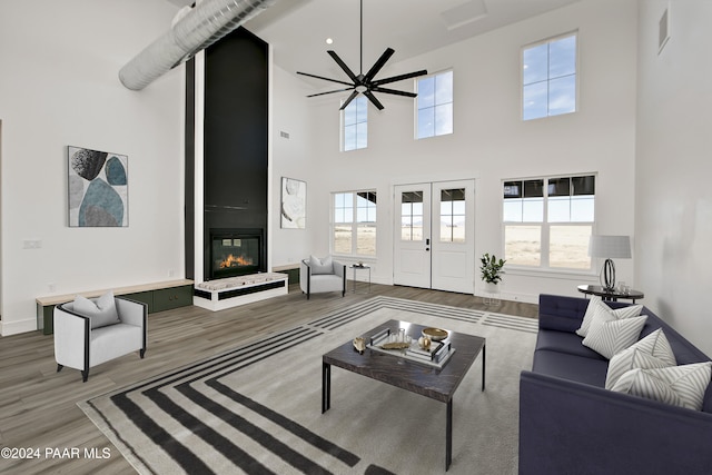 living room featuring ceiling fan, a large fireplace, hardwood / wood-style floors, and a towering ceiling