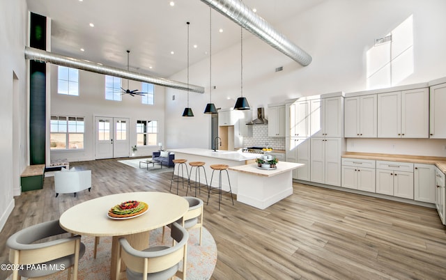 kitchen featuring ceiling fan, pendant lighting, a high ceiling, a kitchen island with sink, and white cabinets