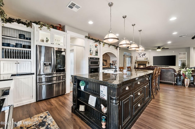 930 S Kerasi Ct, Dewey-Humboldt, AZ 86327 - kitchen with appliances with stainless steel finishes, a lit fireplace, a ceiling fan, open shelves, and a kitchen island