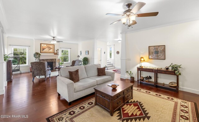 living area with ceiling fan, a fireplace, wood finished floors, baseboards, and stairs