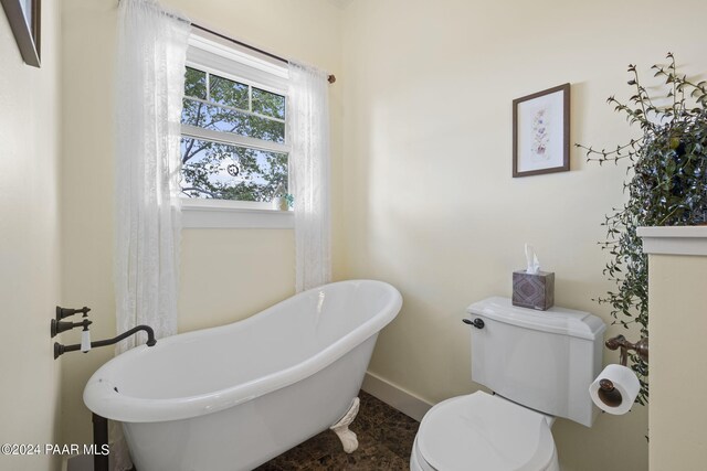 bathroom with a soaking tub, toilet, and baseboards