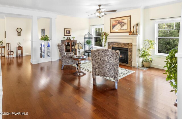 living area featuring a fireplace, wood finished floors, a ceiling fan, decorative columns, and crown molding