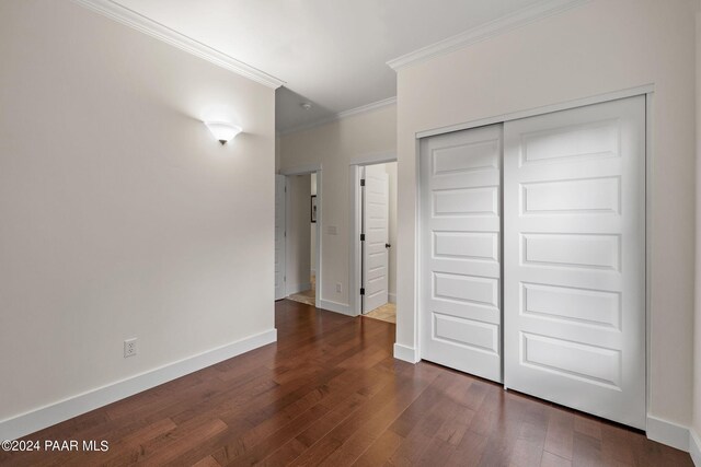 unfurnished bedroom with a closet, dark wood-style flooring, crown molding, and baseboards