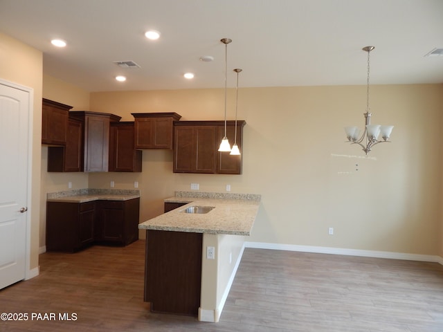 kitchen featuring hanging light fixtures, light stone counters, light hardwood / wood-style floors, and kitchen peninsula