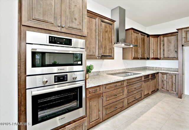 kitchen featuring light tile patterned floors, wall chimney exhaust hood, light stone counters, black electric stovetop, and stainless steel double oven