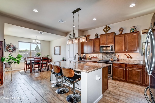 kitchen with pendant lighting, an island with sink, stainless steel appliances, and sink