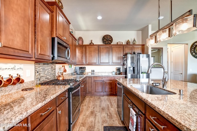 kitchen with light stone countertops, sink, stainless steel appliances, light hardwood / wood-style flooring, and decorative light fixtures