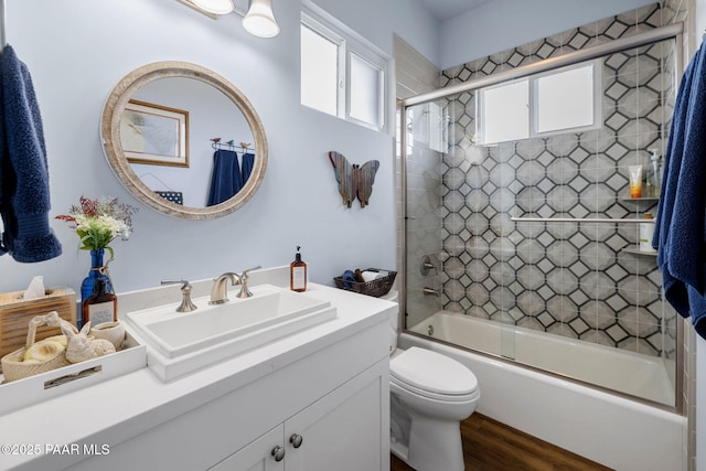 full bathroom with bath / shower combo with glass door, hardwood / wood-style floors, toilet, and vanity