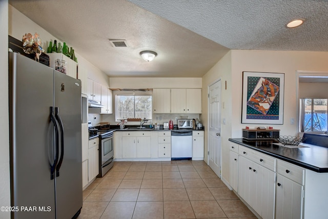 kitchen featuring stainless steel electric range, dark countertops, visible vents, freestanding refrigerator, and dishwashing machine