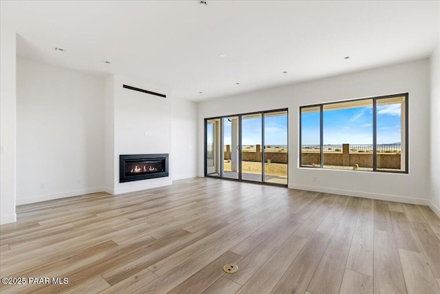 unfurnished living room featuring a wealth of natural light, light wood-type flooring, a glass covered fireplace, and baseboards