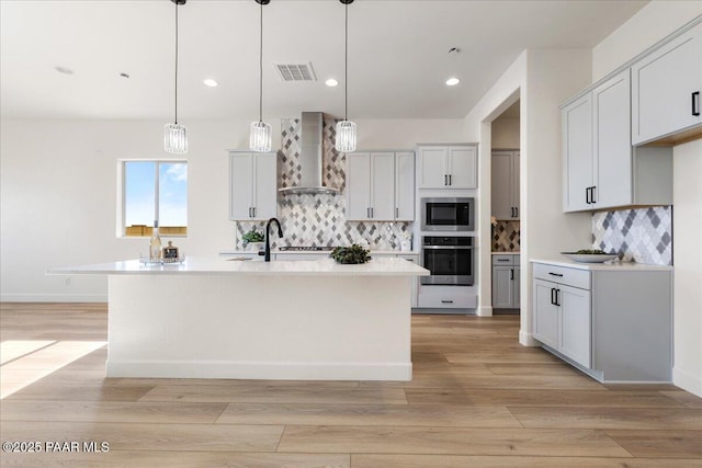 kitchen featuring visible vents, light countertops, appliances with stainless steel finishes, light wood-type flooring, and wall chimney exhaust hood