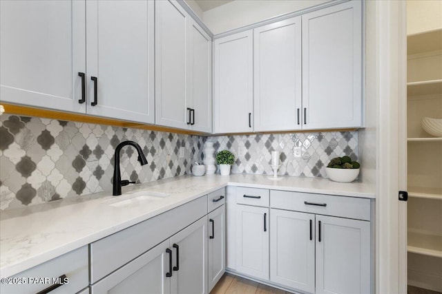 kitchen featuring tasteful backsplash, light stone counters, and a sink